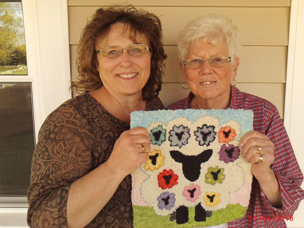 Kim Hirt and Pat Mensing holding the "Because of EWE" rug.